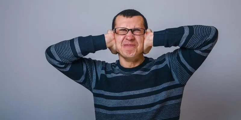 Man covering ears with hands, eyes closed.