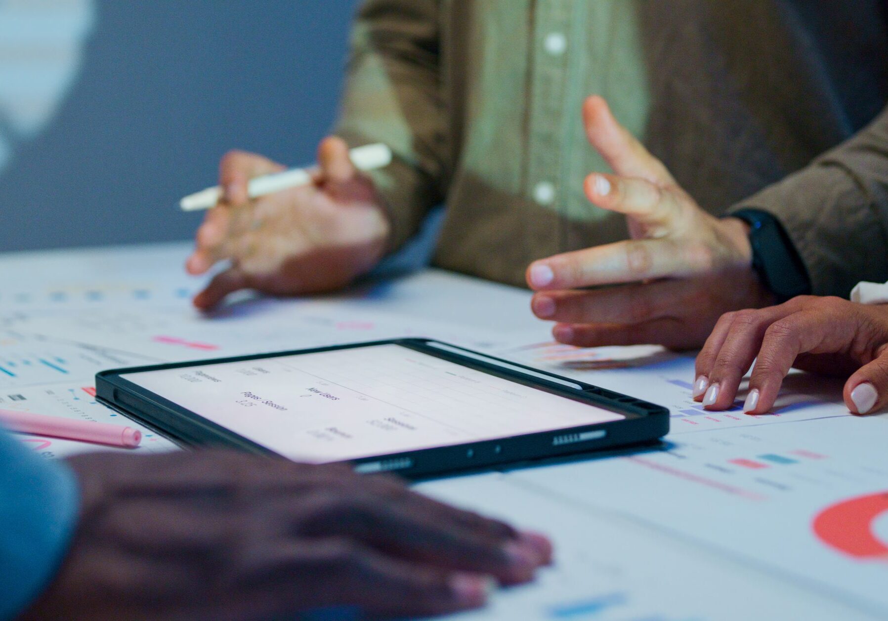 Close-up group of business working late, analyzing financial reports and charts on digital tablet surrounded by documents and graphs during strategic meeting at office night. Finance meeting concept.