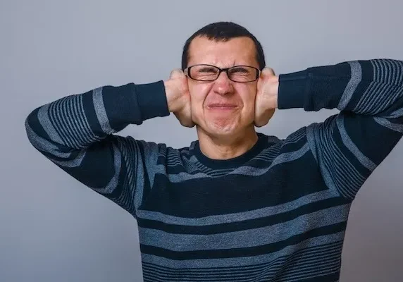 Man covering ears with hands, eyes closed.